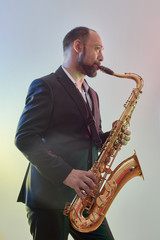 Portrait of professional musician saxophonist man in suit plays jazz music on saxophone, white background in a photo studio, side view