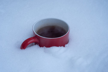 Buried in snow Red mug with Steaming hot black hot tea or cup of mulled wine.