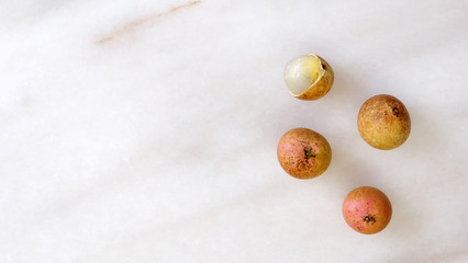 Top view of longan fruits on a marble surface, with empty space on the left. Longan is an edible tropical fruit that is commonly found in traditional Eastern folk medicine.