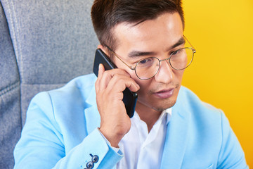 Asian handsome Kazakh businessman in a suit and glasses works in the office, a successful professional serious manager solves business issues by mobile phone