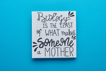 top view of card with biology is least of what makes someone mother lettering on blue background