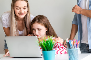 Young girl using laptop with parent guiding her. White girl with mother and father giving guidence...