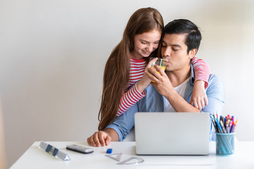 Father working at home with children around him. White man and girl, drinking orange juice, happy laugh.