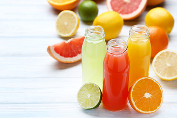 Citrus juice in glass bottles with fruits on white wooden table