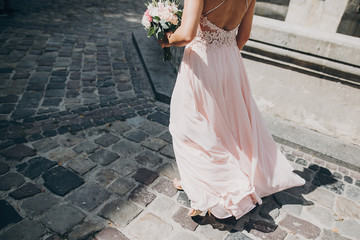 Stylish bridesmaid in pink dress walking in european city street and holding wedding bouquet,...