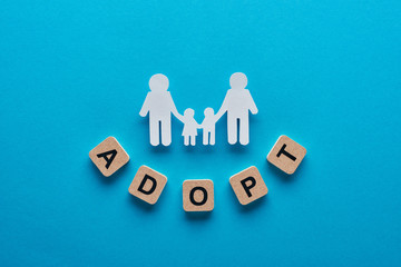 top view of paper cut gay family holding hands on blue background with adopt word on wooden cubes