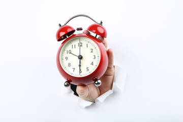 Hand holding alarm clock from white torn paper