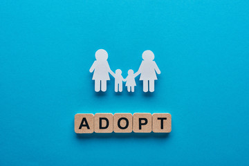 top view of paper cut lesbian family holding hands on blue background with adopt lettering on...