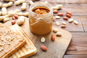 Peanut butter with bread and nuts on wooden table