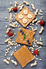 Bread with peanut butter, fruits and nuts on wooden table
