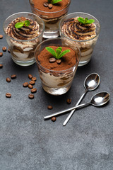 Classic tiramisu dessert in a glass cup on dark concrete background