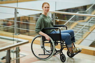 Fototapeta na wymiar Portrait of young red-haired woman sitting in wheelchair and looking at camera she is a patient at modern hospital