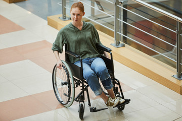 Young red-haired female patient going on wheelchair along the corridor at hospital