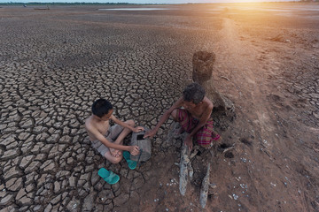 Fototapeta na wymiar Global warming and water crisis,Local Asian grandfather and child sitting with fishing tools on drought land.Climate Change