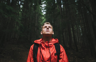 Portrait of a handsome young man in a red jacket stands in the evening forest with his head up,...