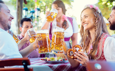 Couple clinking glasses with huge amounts of beer in Bavarian pub - obrazy, fototapety, plakaty