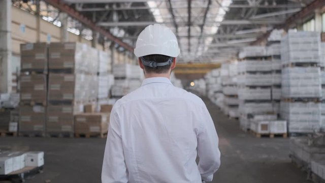 Follow footage of employees male warehouse worker engineer in hard hat working. walking through logistics center warehouse factory construction site logistics architect businessman man builder indoors