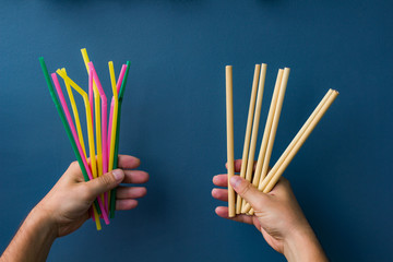One hand holds colourful plastic straws and another hand holds bamboo straws. Good background for ecology topics.