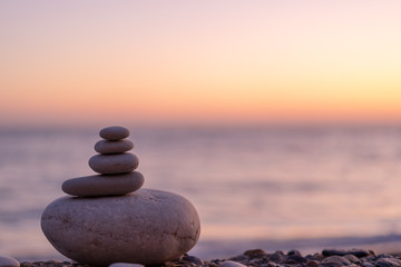 Perfect balance of stack of pebbles at seaside towards sunset. Concept of balance, harmony and meditation. Helping or supporting someone for growing or going higher up. - obrazy, fototapety, plakaty