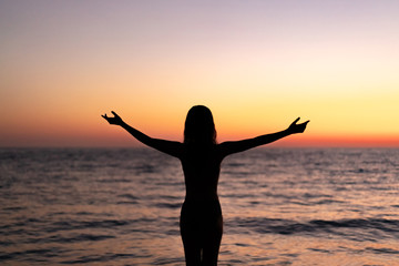 Silhouette of beautiful young gracile pensive woman with a freedom feeling  rise hand up on beautiful sunset. Freedom and travel adventure happy feeling concept.