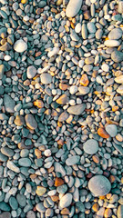 Abstract background of small pebbles lit by the sun. Pebble texture with a blue tint. Stone background. Pebble beach with multi-colored stones. Turquoise. Vertical frame