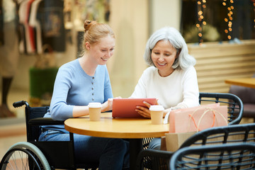 Mother and daughter watching something on digital tablet and smiling while sitting in cafe after shopping
