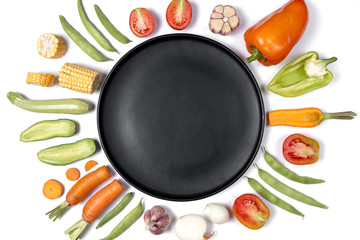 Creative layout made of haricot, tomatoes, pepper, carrot, garlic, corn, zucchini, onion and black plate. Organic food background. Flat lay, top view, copy space. Healthy eating concept.
