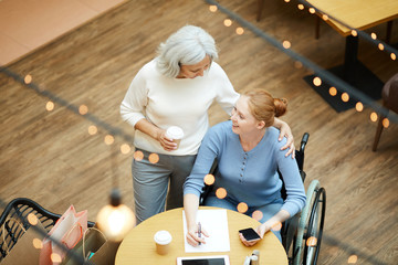 Senior woman with coffee cup standing and talking to young woman while she sitting at the table...