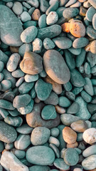 Abstract background of large pebbles. Pebble texture with a blue tint. Stone background. Pebble beach with multi-colored stones. Turquoise. Vertical frame