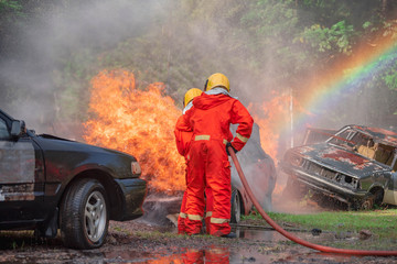 Firefighter in fire fighting suit using water and extinguisher to fighting with huge  fire flame in accident burning car  on the wayside road.