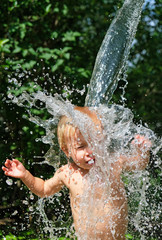 Fototapeta premium Funny little kid is poured with cold water from bucket. Water games on hot day in backyard. Hardening for health. Strengthen your body. Staying cool in summer