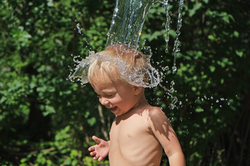 Fototapeta na wymiar Small cute child is poured with cold water from bucket. Water games on hot summer day in backyard. Hardening for health. Strengthen your body. Staying cool.