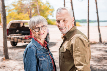 smiling senior couple looking at camera in forest in sunny day