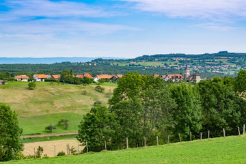 Fototapeta na wymiar Hilly and picturesque landscape view of meadows, pastures, fields, trees, town of Brens and white clouds in the blue sky.Department of Haute-Savoie,region of Auvergne-Rhone-Alpes in France.