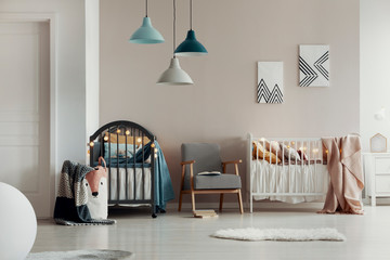 Real photo of a spacious, white and beige bedroom interior for twins with two wooden cribs and an...