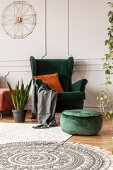 Comfortable emerald green armchair with orange pillow in fashionable living room interior