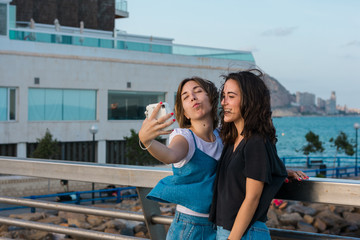 Two young women are taking a selfie with a instant camera in the coast