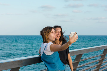 Two young women are taking a selfie with a instant camera in the coast