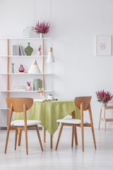 Chairs at table in elegant dining room with heather in pots and accessories on shelf , real photo