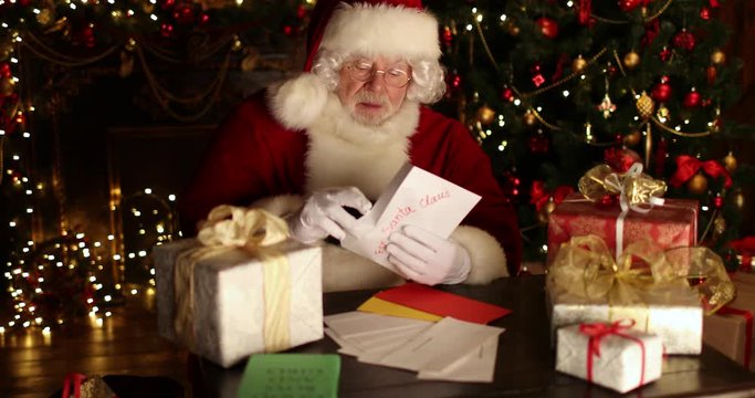 Santa Claus  is sitting at the table, reading letter and smiling in a room decorated for Christmas. Christmas and New Year time. 