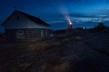 Stone church with lighthouse beam in background at dusk