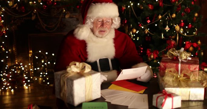 Santa Claus  is sitting at the table, reading letters and chooses gifts for children in a room decorated for Christmas. Christmas and New Year time. 