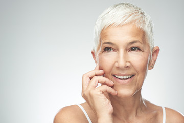 Beautiful smiling senior woman with short gray hair posing in front of gray background. Beauty photography.