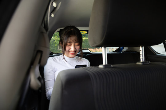 Asian Teenager Woman Using A Smartphone In Back Seat Of Car, Passengers Use An App To Order A Ride And Peer-to-peer Ride Sharing Concept