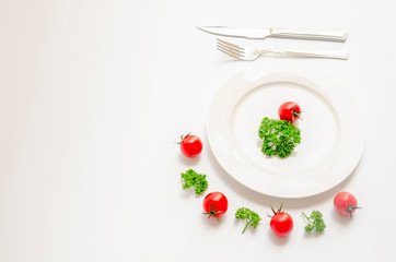 Close up top view of green parsley and red tomato on white dish with knife and fork with copy space on white background, Diet food, vegan and  vegetarian food concept.
