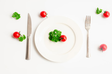Close up top view of green parsley and red tomato on white dish with knife and fork with copy space on white background, Diet food, vegan and  vegetarian food concept.