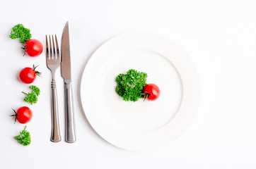 Close up top view of green parsley and red tomato on white dish with knife and fork with copy space on white background, Diet food, vegan and  vegetarian food concept.