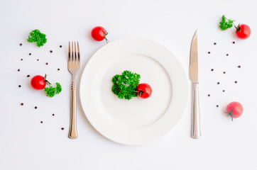 Close up top view of green parsley and red tomato on white dish with knife and fork with copy space on white background, Diet food, vegan and  vegetarian food concept.