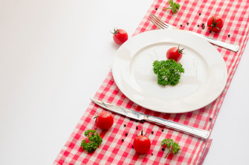 Close up top view of green parsley and red tomato on white dish with knife and fork with copy space...