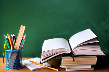 School supplies, stack of books, chalk board and open book on a wooden surface, selective focus